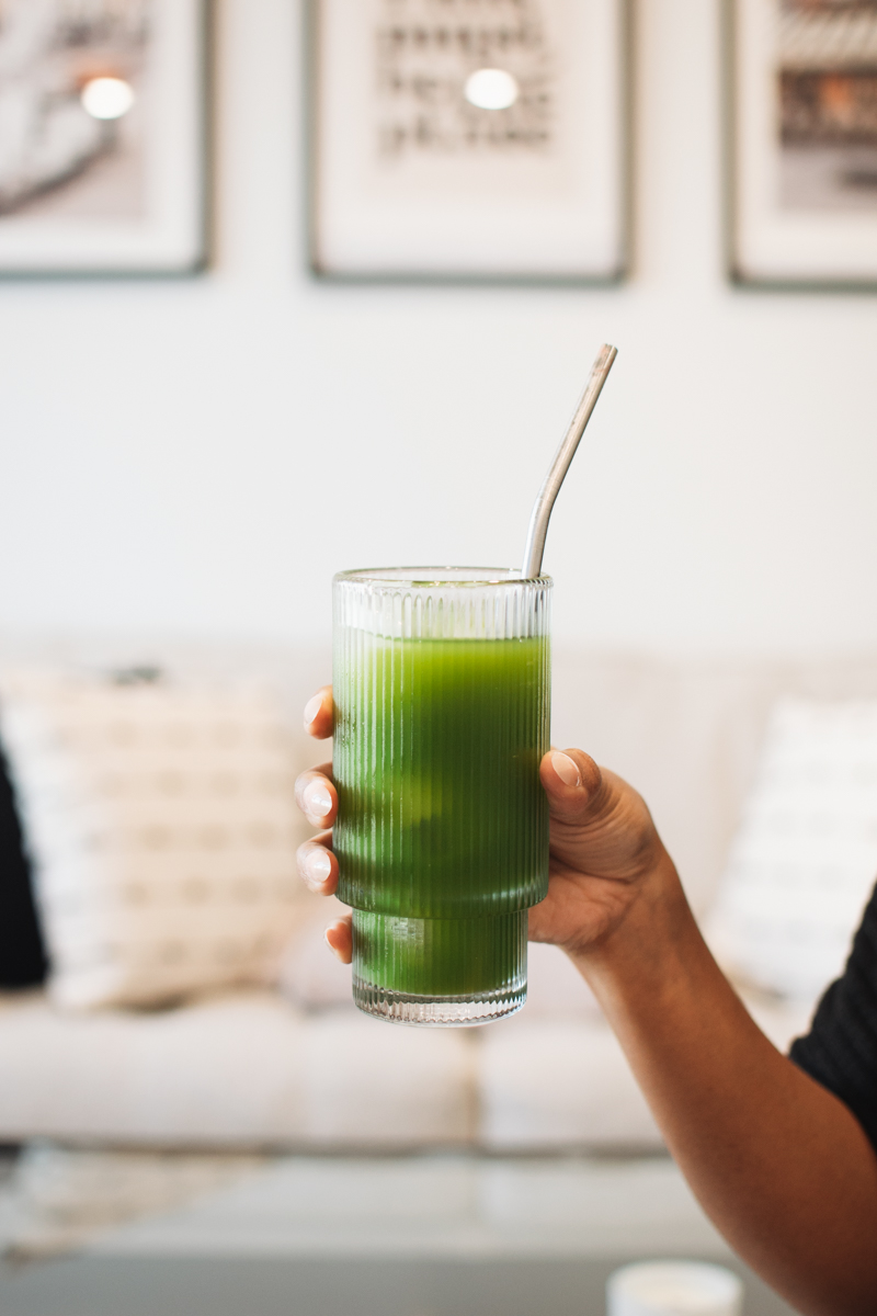 This image shows a glass of freshly made green juice held by my hand in the shot and the background blurred